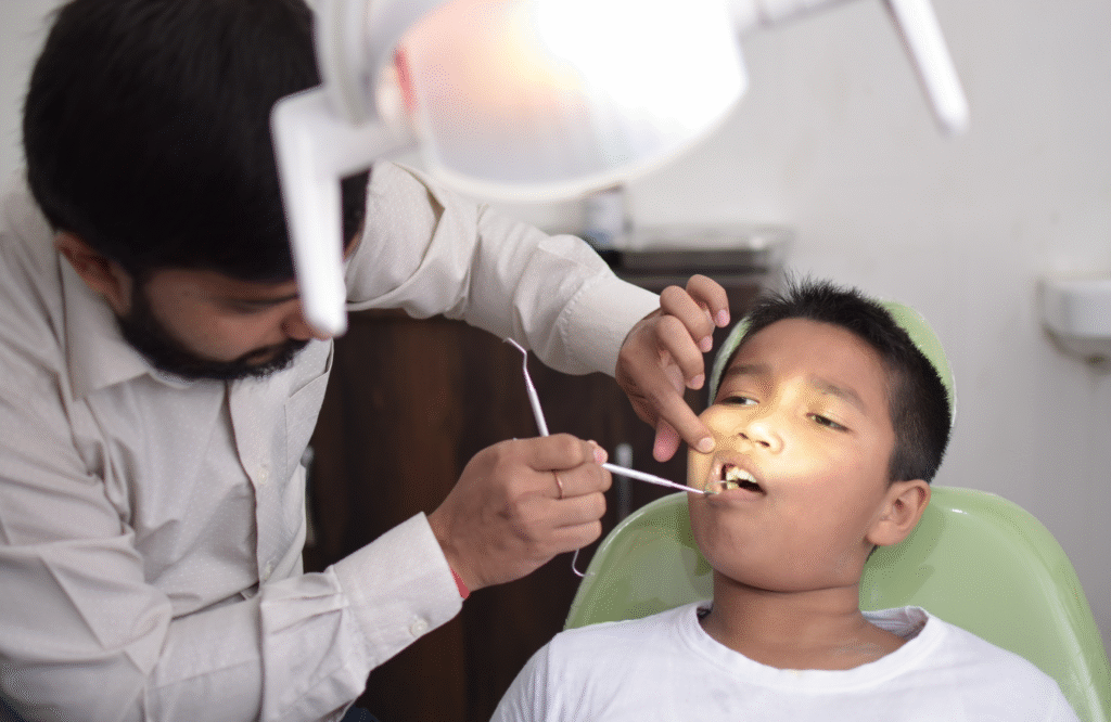 A dentist examining and treating the teeth of a young boy in a dental chair under bright light — Saving Smiles How We Treated Severe Cavities in an 8-Year-Old.