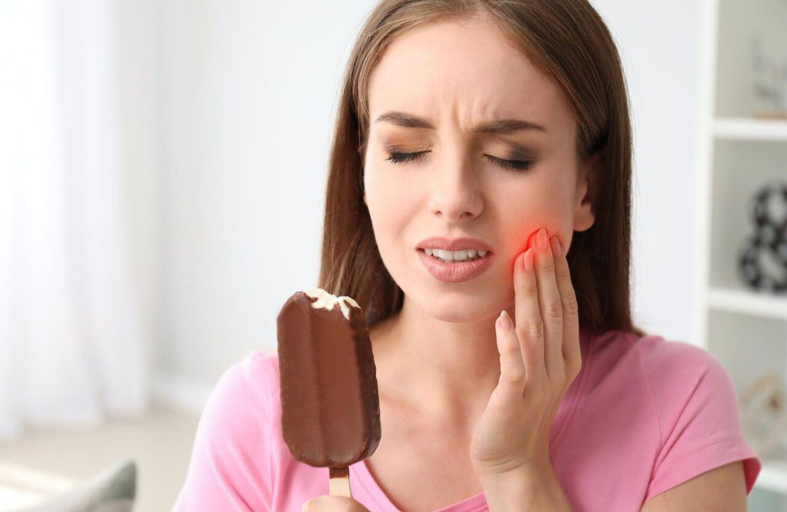 Sensitive Teeth: Reasons for Pain & How to Get Better – Woman experiencing tooth sensitivity while eating ice cream | Core Dental